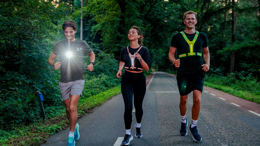 Drie hardlopers op een boswegje in de schemering, met borstlamp en LED-vesten voor zicht en zichtbaarheid