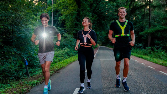 Drie hardlopers op een boswegje in de schemering, met borstlamp en LED-vesten voor zicht en zichtbaarheid